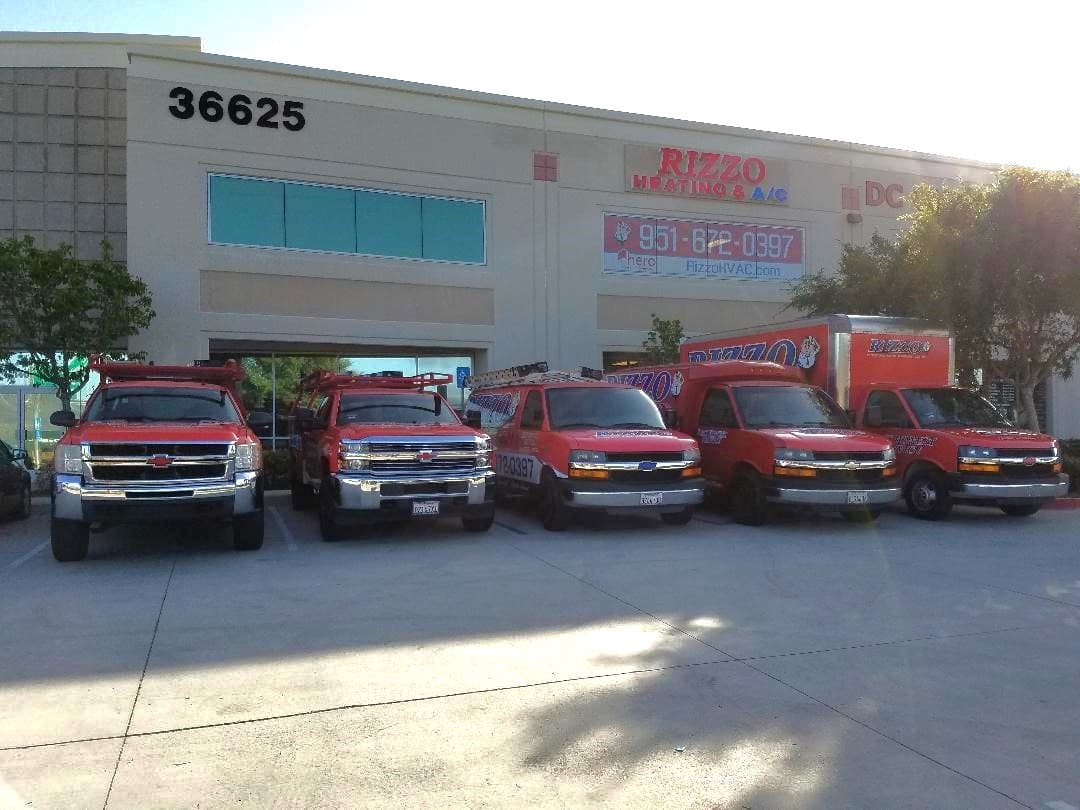 Five red Rizzo service trucks lined up in front of the Rizzo Heating and Air Conditioning shop